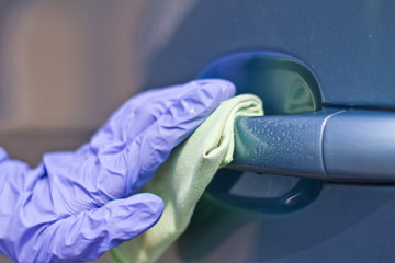 Man's hand in protective gloves cleaning car door handle using antibacterial or cleaning solution