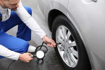 Wall Mural - Mechanic checking tire pressure in car wheel at service station, closeup