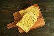 Top View of Two Garlic Butter Toasts on Wooden Plate Served on Dark Brown Table