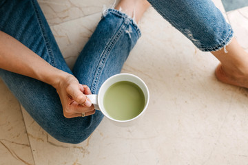 Close-up of a woman sitting on the floor, drinking matcha tea.