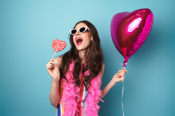 Wall Mural - Photo of delighted young woman posing with balloon and lollipop