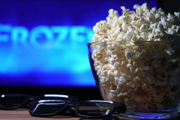 glass bowl of popcorn and 3D glasses in the background a TV is running. In the evening, we watch movies sitting at home on self-isolation due to the covid-19 pandemic.