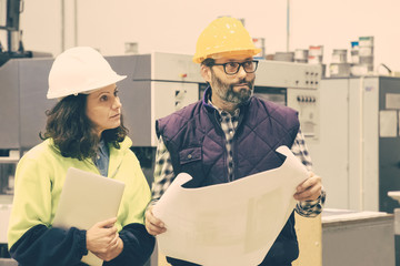 Wall Mural - Two printing workers with blueprints. Focused employees holding blueprints and laptop and looking aside. Print manufacturing concept