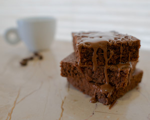 A stack of choclate brownies dripping choclate on marble background with espresso and coffee beans