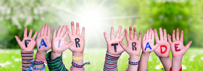 Children Hands Building Colorful Word Fair Trade. Sunny Green Grass Meadow As Background