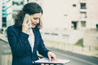 © Mangostar - Businesswoman talking by smartphone and looking at papers. Focused middle aged businesswoman talking via cell phone and looking at folder with documents on street. Business concept