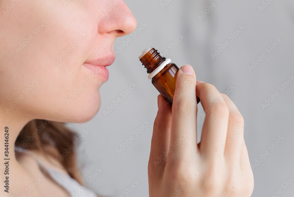 Aromatherapy: a girl with beautiful skin holds a bottle of essential oil near her nose and inhales. Close up, bright marble background. - obrazy, fototapety, plakaty 
