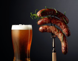 Beer and grilled Bavarian sausages with rosemary. Sausages on a fork sprinkled with rosemary.