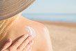 Man hand applying sunscreen lotion on young woman back. Skin protection. Safety sunbathing in hot day at beach. Straw hat on girl head. Closeup.