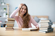 © BestForYou - Happy young woman sits at a table with books at home.
