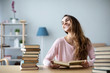 © BestForYou - Happy young woman sits at a table with books at home.