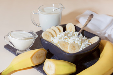 Food, balanced nutrition, healthy diet protein breakfast made from dairy and fruit. Fresh calcium source of homemade cottage cheese in a bowl with sliced banana milk cream sour cream and yogurt