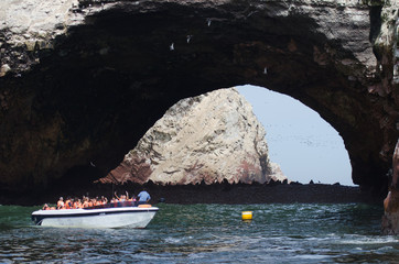 Barca de turistas bajo un arco de piedra en las Islas Ballestas, Peru