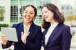 © Mangostar - Businesswomen having video chat outdoors. Cheerful female colleagues standing on city street and talking via tablet pc. Communication concept
