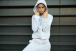 © evgennish - Athletic girl posing in an urban city. The model has a light tracksuit, hood, sneakers. Stylish sports shooting on the street. A beautiful athletic body, face, skin, lips. A girl with a menacing look.