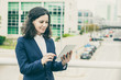 © Mangostar - Smiling woman using tablet computer. Content middle aged businesswoman using digital tablet while standing on urban city street. Wireless technology concept