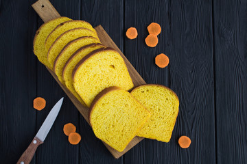 Wall Mural - Homemade carrot bread on the cutting board on the black  wooden background. Top view. Copy space.