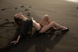 © evgennish - Beautiful sexy girl model lies on black sand beach, in a black swimsuit, with a tanned body, long blonde hair, magnificent breasts and puffy lips. Healthy nature, ocean waves, clouds on Bali island.