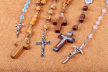 Lots of different styled Christian crosses, multiple rosaries laying on brown background Prayer and belief, christianity symbols abstract concept, group Chaplet of Divine Mercy, rosary prayer symbolic