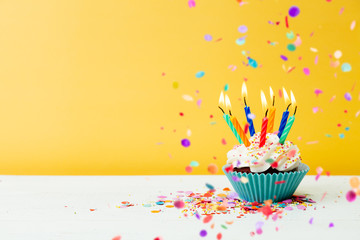 Birthday cupcake with many candles and confetti on yellow background