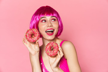 Wall Mural - Image of young party girl wearing wig smiling and holding donuts