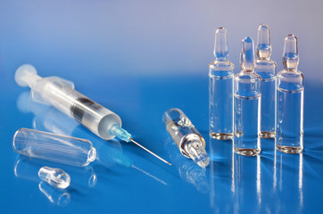 Ampoules with vaccine and a medical disposable syringe on a blue background close-up. Shallow depth of field, selective focus. Concept of health care.