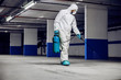 © Dusan Petkovic - Worker in sterile uniform and mask walking trough underground garage and sterilizing surface. Protection from corona virus / covid-19 concept.