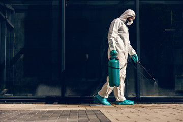 Wall Mural - Full length of man in sterile uniform and mask sterilizing surface outdoors from corona virus, fungus and disease.