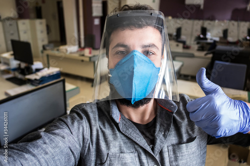 Self portrait of man with mask and protective screen in office