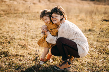 Mother and daughter playing outside on a sunny day. Mother hugging child, having fun together.