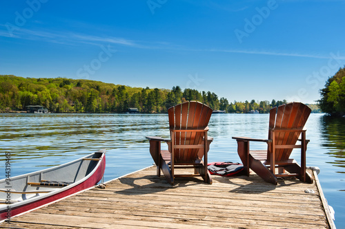 Fotografía Two Adirondack chairs on a wooden dock on a lake in Muskoka, Ontario Canada