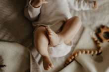 Legs Of A Baby Lying On A Beige Plaid And Wooden Toys On The Background