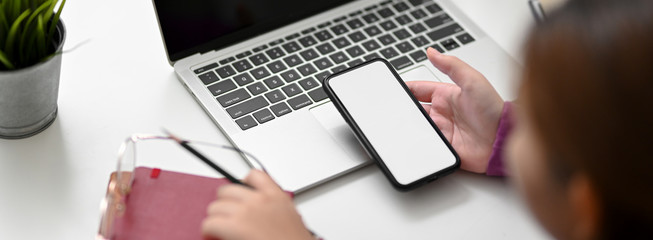 Top view of female college student looking on mock-up smartphone while doing assignment