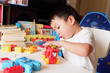 © Kannika - A boy is playing a plastic block on a white table.