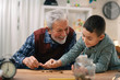 © JustLife - Grandpa and grandson saving money. Grandfather teaching grandchild how to save money.