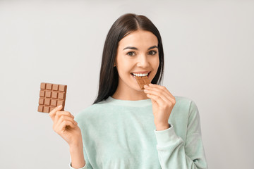 Poster - Beautiful young woman with tasty chocolate on light background