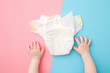 Baby hands and white diaper on light pink blue table background. Pastel color. Closeup. Point of view shot. Top down view. Two sides.
