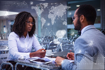 Serious business colleagues discussing ongoing project over cup of coffee. Business man and woman meeting at table with coronavirus geography virtual charts. Global epidemic concept