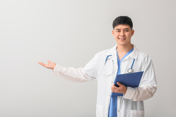 Wall Mural - Male Asian doctor with clipboard showing something on light background