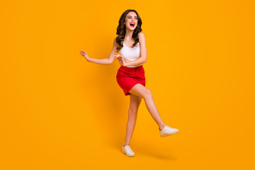 Poster - Full body photo of attractive cheerful lady good mood raise leg hands laughing resting students party wear white casual singlet red mini skirt shoes isolated yellow color background