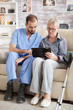 © DC Studio - Young doctor reading diagnostic on tablet for senior woman in nursing home.