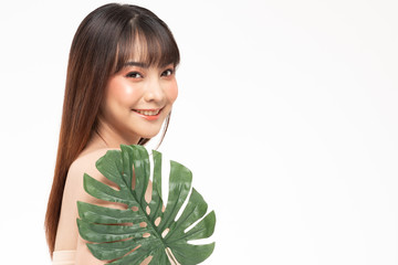 Beauty asian woman  brown hair looking smile in camera happiness and holds a large green tropical leaf in hands and covers a part of her face and cheerful with make up brush,Beauty Concept.