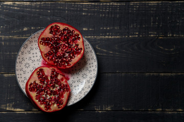 Two halves of pomegranate fruit on plate on black wooden background. Copy space