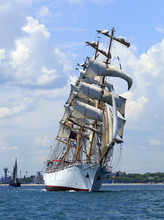 White Sailing Ship With Prominent Sails Against A Blue Sky With White Clouds.