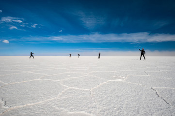 Young tourists playing with perspective at Uyuni Salt Flats (Spanish: Salar de Uyuni) in Bolivia, South America sunny cold day. Salt lake, largest salt flat in the world, altiplano, Uyuni Saline