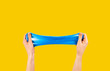 Blue slime stretchable toy for children in hands. An elastic antistress toy for relaxation. Hands gum. Funny Games. Slime on yellow background. Copy space, place for text.