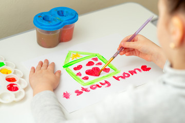 Wall Mural - Child is drawing heart inside house on white sheet of paper with words Stay Home. Stay Home concept.