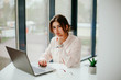 © Катя Іваськевич - young businesswoman working on laptop in the office. portrait of businesswoman. working in the office. happy business woman talking on the phone in the workplace. focused woman working.