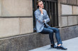 © Alexander Image - Young European Businessman traveling in New York City, wearing gray blazer, black pants, leather shoe, sitting on big window frame on street, frowned, sad, talking on cell phone,  taking work break, .