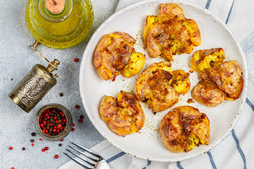 Wall Mural - Baked whole crushed and crusty potato with crust sea salt, olive oil, garlic, pepper and thyme in a white plate on a grey concrete background. Roasted smashed potatoes. Australian cuisine dish